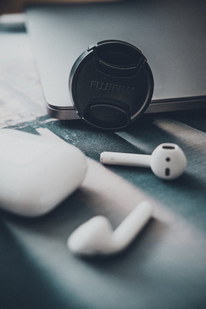 Home Close-up view of wireless earbuds and a camera lens cap on a table indoors.